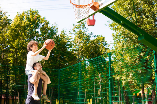 Man holding little boy on shoulders, playing basketball - Photo, Image