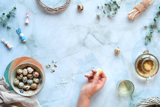 Zero waste Easter background on marble. Quail Easter eggs and natural Spring decorations, twigs and eucalyptus. Green tea in glass teapot, hand holding peeled egg. - Foto, Imagem