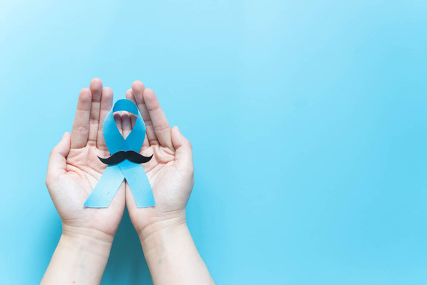 Männergesundheit und Prostatakrebs-Aufklärungskampagne im November. Männerhände mit hellblauem Band und Schnurrbart auf blauem Hintergrund. Symbol für die Unterstützung von Männern, die mit Krebs leben. Kopierraum. - Foto, Bild