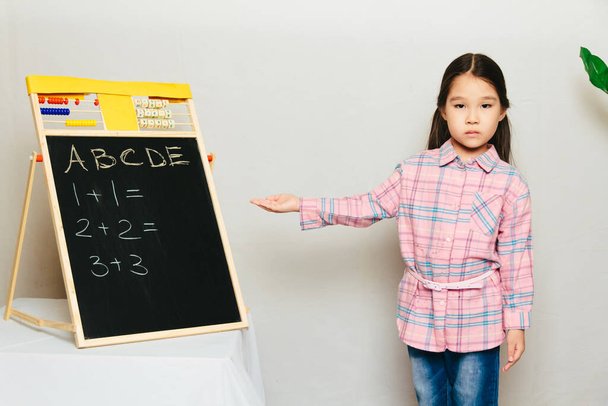 Kleines asiatisches Mädchen zeigt auf Tafel. Bildung zu Hause in Zentralasien, Lektion für Kinder - Foto, Bild
