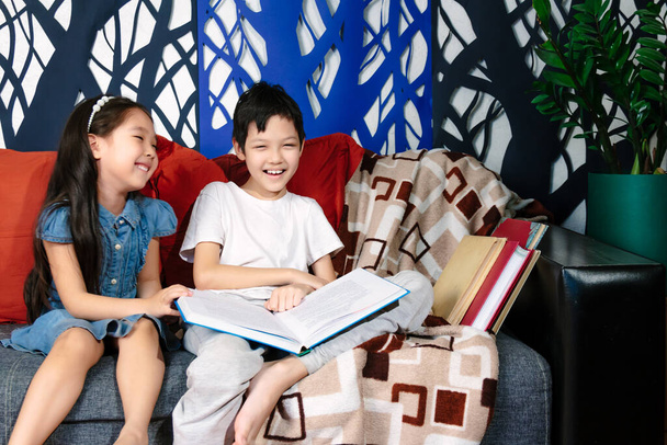 Moments de famille pendant le confinement, enfants lisant un livre assis sur un canapé - Photo, image