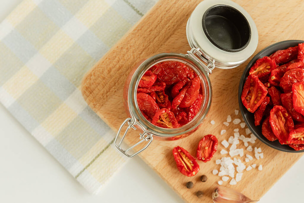 Homemade sun-dried tomatoes in a glass jar, garlic cloves, on a light background. place to copy. selective focus. - Φωτογραφία, εικόνα