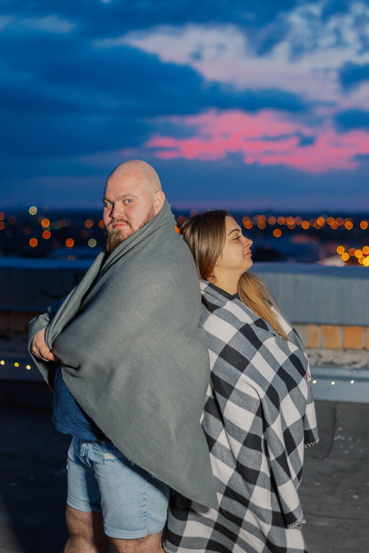 Beautiful couple on the roof under a blanket in the evening. - Photo, Image