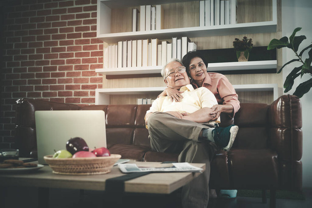 Ηλικιωμένο ζευγάρι αγκαλιάζονται σε έναν καναπέ στο σαλόνι για ευτυχισμένη ηλικιωμένη ζωή. - Φωτογραφία, εικόνα