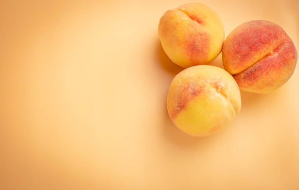 Drie gele perziken op een beige achtergrond. Het uitzicht vanaf de top. - Foto, afbeelding