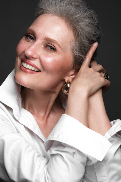 Porträt einer schönen älteren Frau in einem weißen Hemd mit klassischem Make-up und grauen Haaren. - Foto, Bild