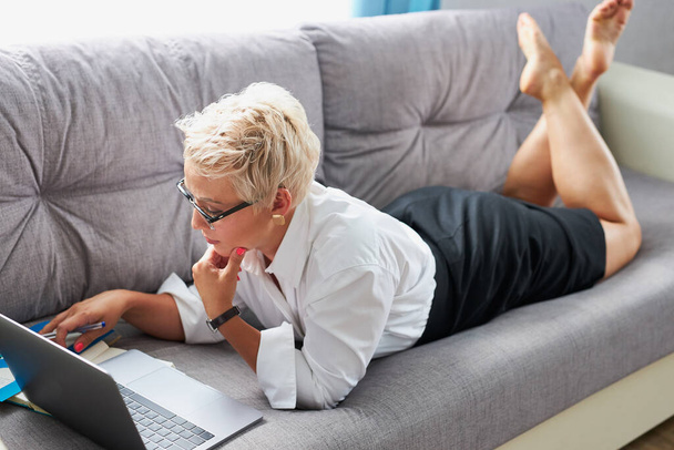 young caucasian teacher tired to sit on sofa with laptop, she is lying - Foto, Imagem