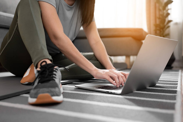 Mujer joven deportista practicando ejercicio con computadora portátil en la habitación. - Foto, imagen