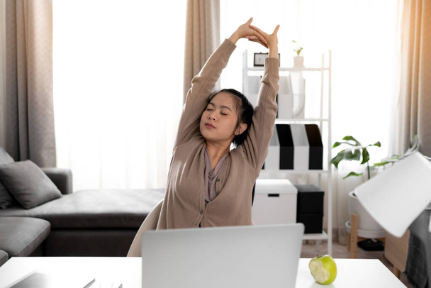 Nuori nainen venyttely työskenneltyään kannettavan tietokoneen kotona. - Valokuva, kuva