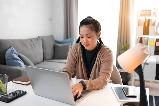 Молодая азиатка работает дома с ноутбуком. - Фото, изображение