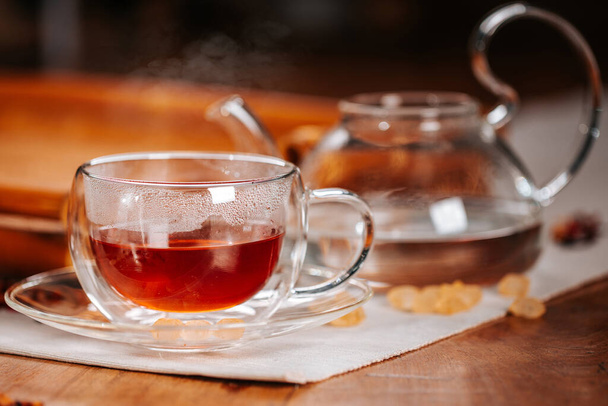 Чашка горячего чая с сахаром из камня, сухие чайные листья в чашке чая из термостекла - Фото, изображение