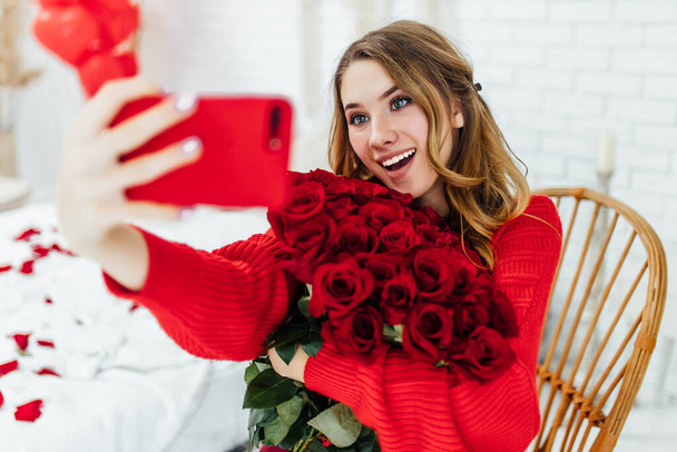 cheerful young woman taking selfie on smarthone, holding bouquet of red roses on smartphone - Foto, Bild