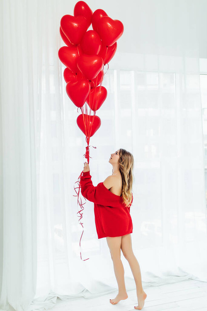 full length shot of cute girl holding heart shaped balloon, standing at the window in the room - Fotografie, Obrázek