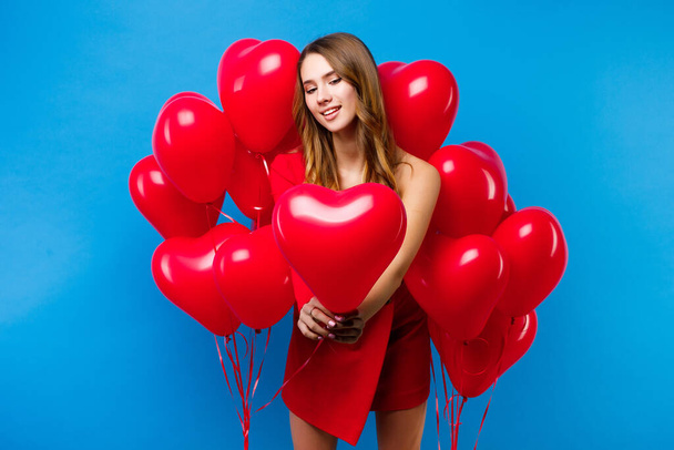 біла дівчина стоїть навколо повітряних кульок у формі серця на синьому фоні
 - Фото, зображення