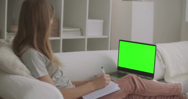 écolière regarde leçon en ligne sur ordinateur portable avec écran vert pour chroma technologie clé, écriture au cahier d'exercices, apprendre de la maison - Séquence, vidéo