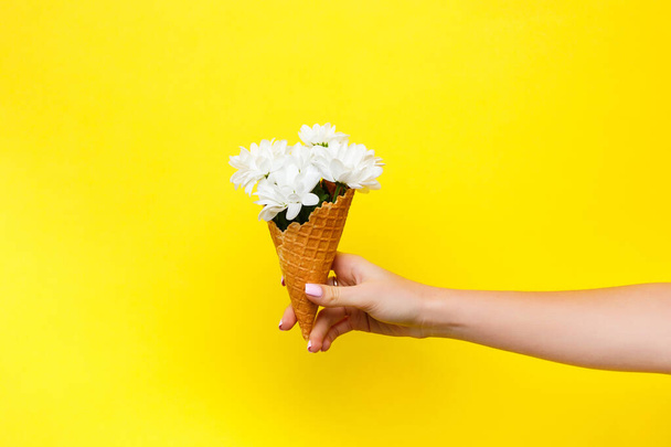 close up of woman hand holding flowers in ice cream cone on yellow background - 写真・画像