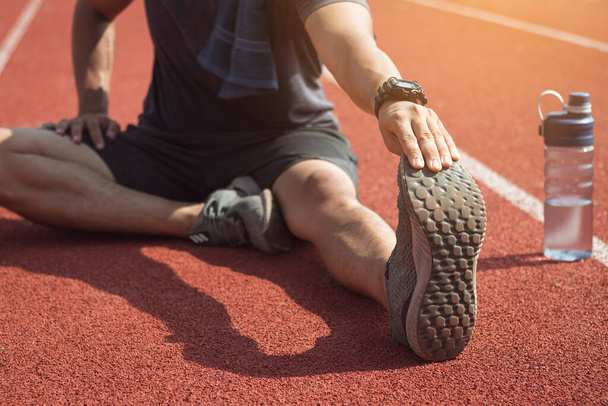 Runner man is stretching legs preparing for run training on track. - Photo, Image