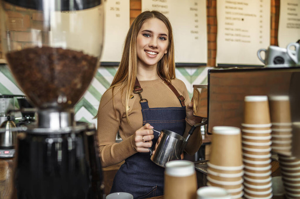 Professional girl barista holding metal jug warming milk using the coffee machine. - Photo, Image