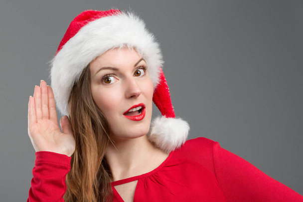 Nuori nainen joulupukin hattu on kätensä hänen korvaansa ja yrittää kuunnella - Valokuva, kuva