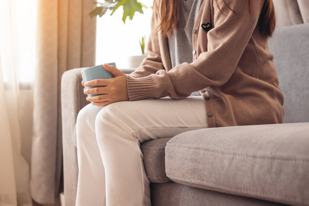 Junge Frau hält Kaffeetasse und sitzt auf Sofa. - Foto, Bild