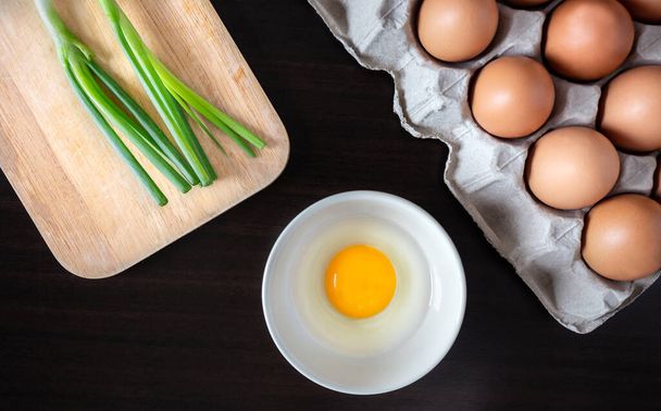 closeup spring onion on wood butcher and fresh chicken egg in bowl and group of egg in box on wooden kitchen table for healthy and delicious meal or food cook concept - Foto, immagini