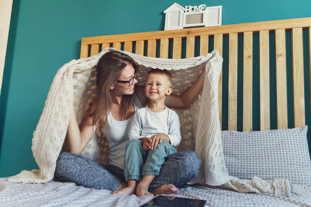 mom and child have fun in the bedroom on the bed, play under the blanket - Foto, Imagem
