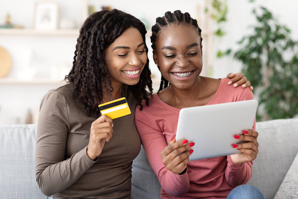Ευτυχισμένα μαύρα κορίτσια ψώνια σε απευθείας σύνδεση, χρησιμοποιώντας ψηφιακή ταμπλέτα στο σπίτι - Φωτογραφία, εικόνα