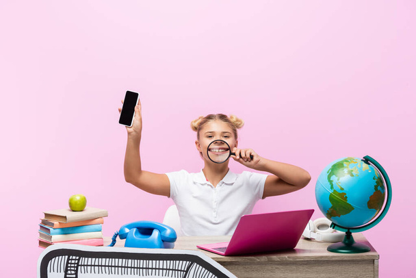 Schulkind hält Smartphone und Lupe in Globusnähe und Papier-Kunstwerk isoliert auf rosa  - Foto, Bild
