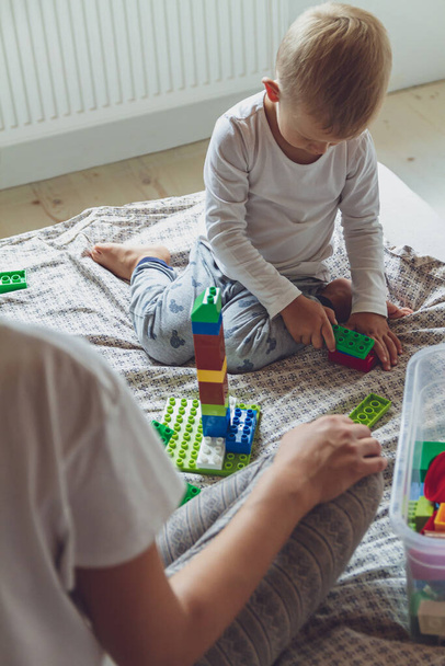 Mom and kid play together in the bedroom on a bed with plastic blocks - 写真・画像