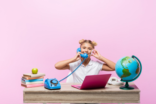 Schoolkid talking on smartphone and telephone near books and globe isolated on pink  - Fotografie, Obrázek