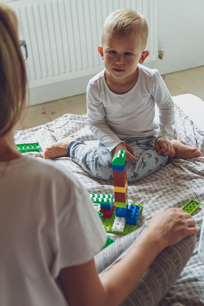 Mom and kid play together in the bedroom on a bed with plastic blocks - Foto, immagini