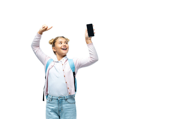 Girl with backpack pointing with finger at smartphone isolated on white  - Foto, imagen