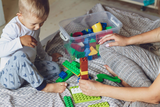 Mom and kid play together in the bedroom on a bed with plastic blocks - Fotoğraf, Görsel