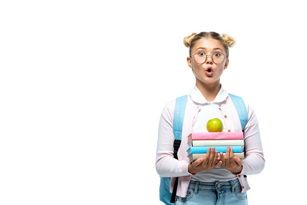 Shocked schoolgirl holding apple and books isolated on white  - Φωτογραφία, εικόνα