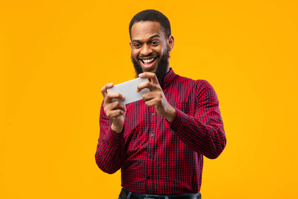 Homme noir excité jouant à des jeux mobiles sur fond jaune - Photo, image