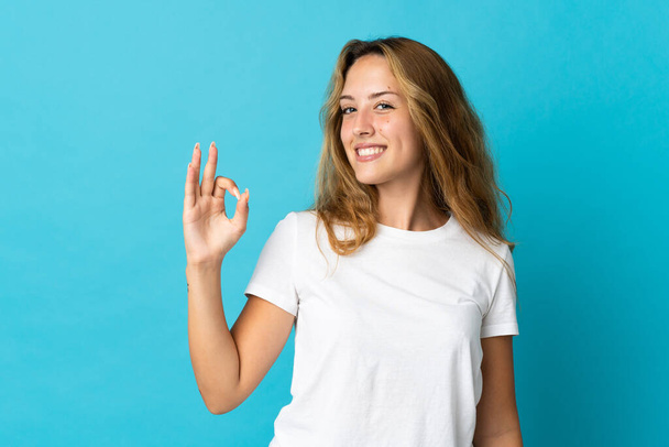 Mujer rubia joven aislada sobre fondo azul mostrando signo de ok con los dedos - Foto, imagen
