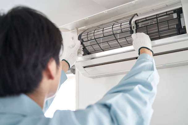 Egy japán férfi villanyszerelő ellenőrzi az otthoni légkondi szűrőit. - Fotó, kép