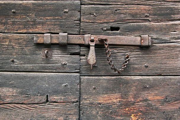 Nahaufnahme einer alten Holztür, die mit einem rostigen Eisenriegel verschlossen wurde - Foto, Bild