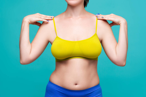 Woman in yellow top bra with big natural breasts on blue background, body positive concept - Foto, Imagen