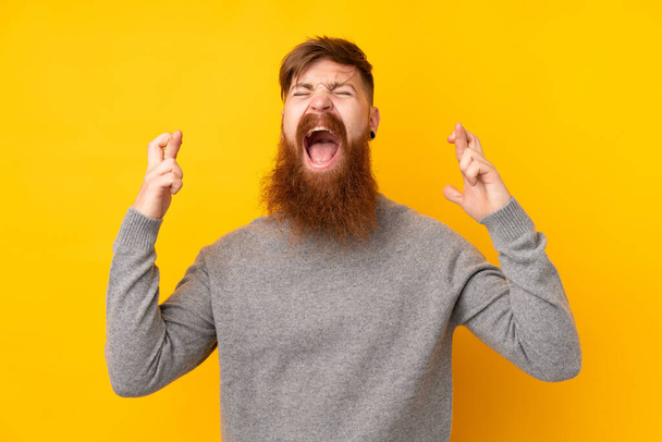 Рыжий с длинной бородой на изолированном желтом фоне со скрещенными пальцами - Фото, изображение