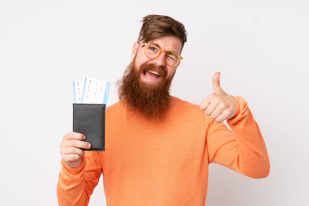 Pelirrojo con barba larga sobre fondo blanco aislado en vacaciones con pasaporte y avión con pulgar hacia arriba - Foto, Imagen