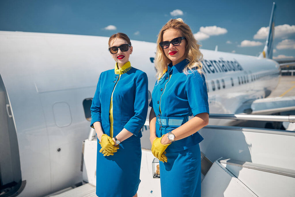 Schöne junge Stewardessen stehen auf Flugzeugtreppen - Foto, Bild