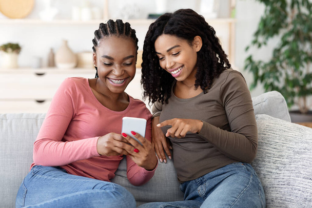 Wesołe afrykańskie dziewczyny oglądające zdjęcia na smartfonie - Zdjęcie, obraz