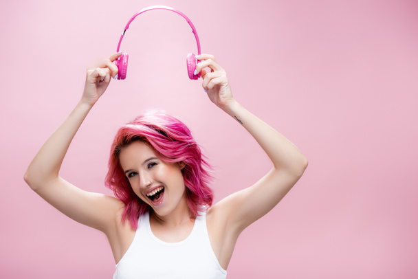 excited young woman with colorful hair holding headphones above head isolated on pink - Fotoğraf, Görsel
