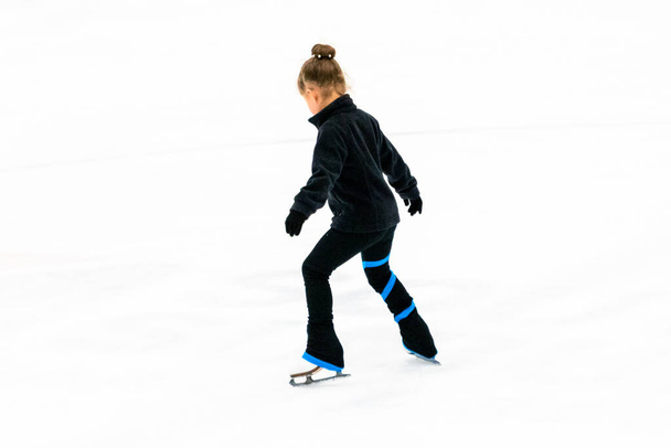 Little figure skater in black clothes practicing on the indoor ice arena. - Photo, Image