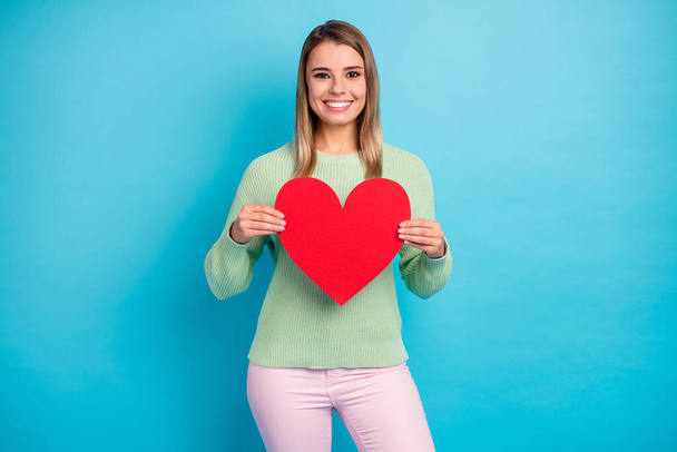 Photo portrait of pretty lovely lady in green sweater holding large red heart isolated over blue background - Fotó, kép