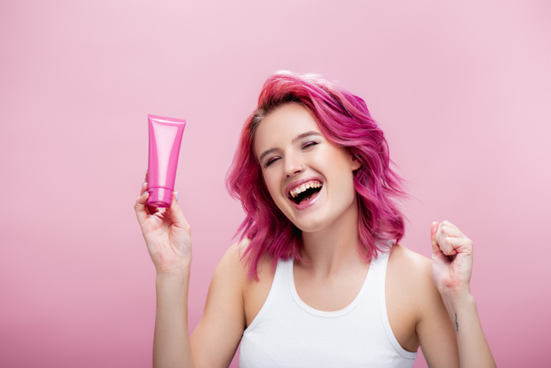 young woman with colorful hair holding tube of cosmetic cream isolated on pink - Fotografie, Obrázek