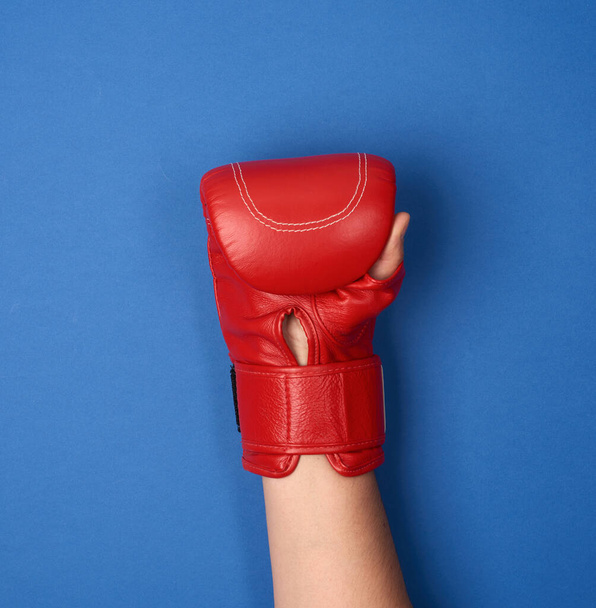 guante de boxeo de cuero rojo en una mano femenina sobre un fondo azul se levanta - Foto, Imagen