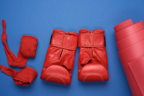 Bir çift kırmızı deri boks eldiveni ve tekstil kırmızısı elastik bandaj. Eller mavi arka planda, spor setinde, düz yerde yatar. - Fotoğraf, Görsel