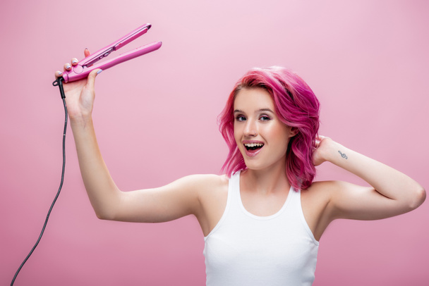 giovane donna con capelli colorati tenendo piastra isolata su rosa - Foto, immagini